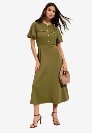 Olive roheline midi kleit padjatsvarrukate, nööbitava eesosa ja kahe rinnataskuga. Ühildatud pruuni punutud käsikotiga ja rihmikute kontssandaalidega.