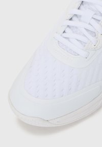Baskets blanches sportives avec une tige en mesh texturé, des superpositions synthétiques lisses, des lacets plats et une semelle en caoutchouc épaisse avec un motif de crampons.