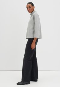 Pull gris clair avec col montant, manches 3/4 et coupe décontractée. Associé à un jean noir à jambes larges et des chaussures en cuir noir.