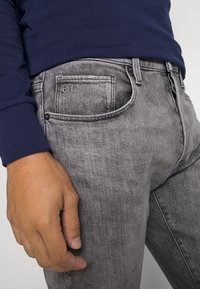 Grå denimjeans med en subtil falmet tekstur, med klassisk fem-lomme-design, metallknapp og brodert logo på baklommen.