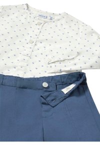 Camisa blanca con lunares azules y un frente con botones, combinada con pantalones cortos azules que cuentan con un cierre de botón y una cinturilla elástica.