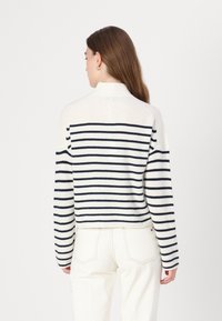 Strikkegenser med høy krage, med marineblå og hvite horisontale striper. Ribbestrikket tekstur og lett cropped design.