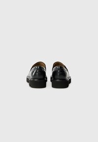 Black leather loafers with a smooth finish, rubber soles, and subtle stitching details. Classic design with a low profile and slip-on style.