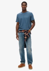 Blå bomulds t-shirt, afslappet pasform, knyttet ternet flannel om livet, falmede blå denim jeans, brune læder bådsko, afslappet outfit.