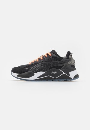 Sneaker Puma nero e grigio con suola bianca, lacci arancioni e motivi geometrici esposti su uno sfondo bianco.