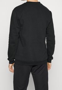 Felpa nera in tessuto liscio con collo rotondo, polsini e vita a costine. Design semplice e minimalista, senza loghi o motivi visibili.