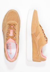 Světlé semišové tenisky s béžovými koženými akcenty, růžovou vnitřní podšívkou a bílou gumovou podrážkou. Mají kulatou špičku a šněrovací design.