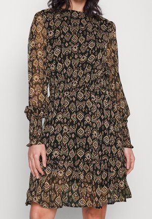 Frau trägt ein schwarzes knieumspielendes Kleid mit einem mehrfarbigen geometrischen Muster, langen transparenten Ärmeln sowie elastischem Bund und Manschetten.