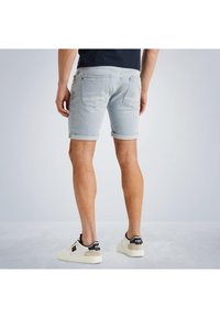 Helle, blaue Denim-Shorts mit umgeschlagenen Säumen, ausgestattet mit Gesäßtaschen und einer glatten Textur. Kombiniert mit weißen Turnschuhen mit schwarzen Akzenten.