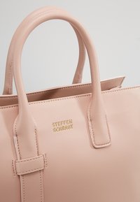 Różowa skórzana torebka z dwoma okrągłymi uchwytami, złotym wytłoczonym logo "STEFFEN SCHRAUT", strukturalny design i minimalne detale w szwach.