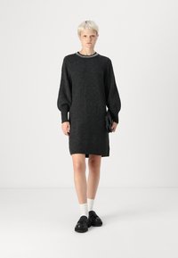 Robe tricotée gris foncé avec des manches ballons, un col rond orné de couture décorative et une coupe ample, associée à des chaussures noires et des chaussettes blanches.