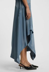 Ein blaues Satin-Kleid mit asymmetrischem Saum, eleganter Drapierung und glatter Textur. Schwarze Slingback-Schuhe mit spitzem Fuß ergänzen das Outfit.
