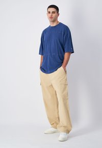 Niebieska bawełniana koszulka oversize z krótkimi rękawami, z poziomą szwem, połączona z beżowymi spodniami cargo i białymi sneakersami.