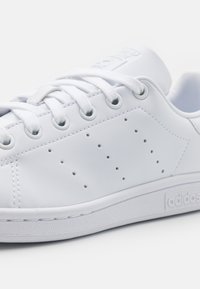 Baskets en cuir blanc avec un bout rond, des lacets plats et de petites perforations sur les côtés. Elles sont dotées d'une semelle en caoutchouc et d'un logo en relief sur la languette.