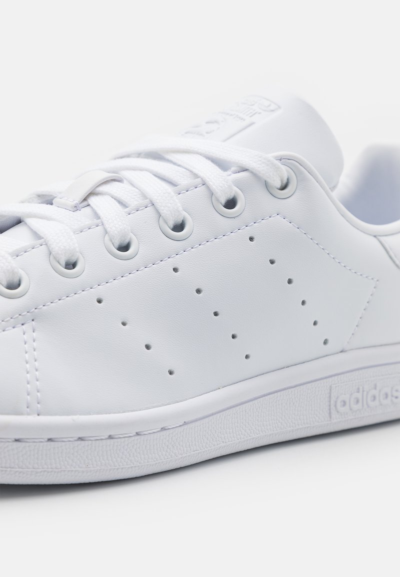 Baskets en cuir blanc avec un bout rond, des lacets plats et de petites perforations sur les côtés. Elles sont dotées d'une semelle en caoutchouc et d'un logo en relief sur la languette.