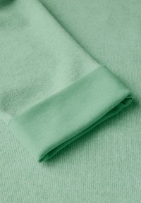 Mintgrön tyg med ribbad textur och en vikt manschett. Slät yta med ett mjukt utseende, som visar en tajt passform.