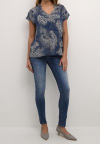 Námořnická blůza s bílým paisley vzorem, krátké rukávy a výstřih do V, zkombinovaná se světle modrými skinny džíny a šedými lodičkami na vysokém podpatku.