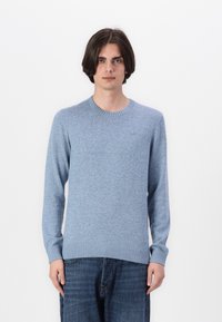 Ljusblå tröja i strukturerad stickad tyg, med rund halsringning och ribbade muddarna och nederkant. Bärs över mörka denimjeans.