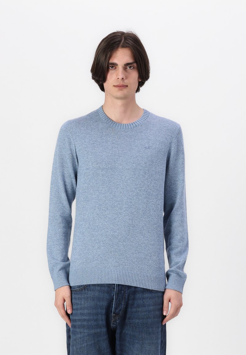 Ljusblå tröja i strukturerad stickad tyg, med rund halsringning och ribbade muddarna och nederkant. Bärs över mörka denimjeans.