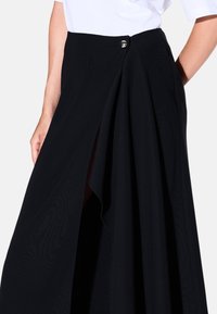 Gonna maxi nera realizzata in tessuto fluido, con uno spacco frontale, chiusura a bottoni classica e una texture liscia con drappeggi sottili.