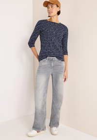 Marineblau gestreiftes Langarmoberteil mit rundem Halsausschnitt, kombiniert mit hellgrauen geraden Jeans und weißen Sneakers.