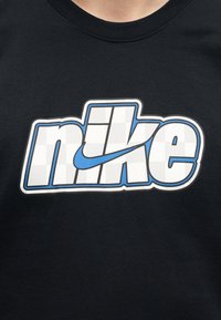 Svart skjorte med en hvit og blå stilisert "nike"-logo med en blå swoosh integrert i teksten på brystet.