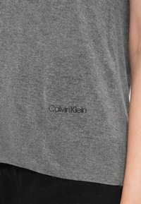 Šedý pletený svetr s jemnou texturou. Obsahuje skryté logo značky v černé barvě, minimalistický design a uvolněný střih.