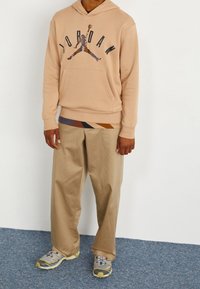 Sudadera con capucha en color beige que presenta un gráfico del logo "Jordan", combinada con pantalones beige y zapatillas deportivas grises con acentos amarillos y cordones.
