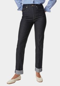 Jeans de mezclilla oscuros de tiro alto con un corte recto, dobladillos acampanados y detalles en dorado. Material de algodón con un ligero estiramiento.