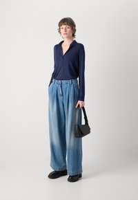 Mornarska polo majica s dugim rukavima u kombinaciji s svijetloplavim farmerkama širokih nogavica. Crna strukturalna torba i masivni crni platformasti cipele.