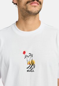 Witte katoenen t-shirt met een kleurrafisch ontwerp van palmbomen, zon en een edelsteen, met zwarte en gele accenten. Weergegeven logo: RVCA.