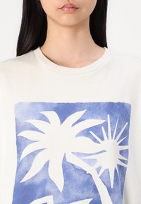 Camiseta de algodón blanca con un diseño gráfico azul de palmeras y un sol. Cuello redondo clásico y mangas cortas. Textura suave.