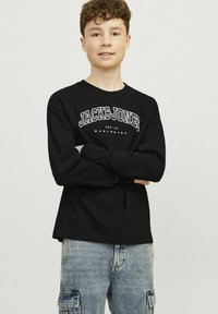 Fekete, hosszú ujjú póló fehér "JACK&JONES" logóval és felirattal az elején, világoskék cargo nadrággal párosítva. Simább anyagtextúra.
