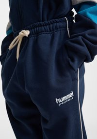 Mörkblå sportbyxor med elastisk midja och kontrasterande vita detaljer, med en framträdande "hummel SPORTSWEAR"-logotyp i vitt.