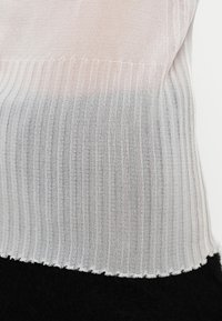 Hvit ribbestrikket topp med en gradient som går over til grå, med en bølget kant og en myk tekstur.