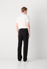 Black trousers with a straight-leg design, featuring back pockets and minimal hardware, paired with a plain white t-shirt.