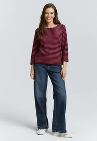 Bordowa bluzka w paski z długim rękawem i okrągłym dekoltem, zestawiona z szerokimi dżinsami o luźnym kroju w niebieskim kolorze. Całość uzupełniona białymi trampkami z płótna.