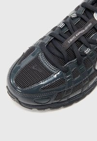 Černá sportovní bota s síťovinou a syntetickými překrytími, černé tkaničky a text "ILL FLOWERMAN SERIES" na jedné tkaničce na bílém pozadí.