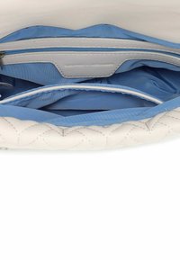 Interno di una borsa bianca trapuntata con fodera blu e una tasca con zip. La fodera è liscia, con una forma elegante e strutturata.