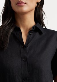 Black button-up shirt in a lightweight fabric with a collar, featuring a front placket with buttons and subtle texture.