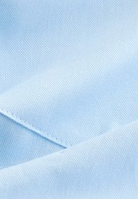 Lyseblåt stof med en glat, struktureret vævning, der viser diagonale folder og pæn syning langs kanterne.