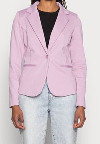 Laventeli, muotoiltu bleiseri, jossa on yhdellä napilla sulku, lovetut kaulukset ja sivutaskut, yhdistetty vaaleaan farkkukankaaseen. Sujuva rakenne.