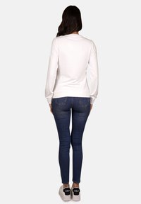 Weißes Langarmshirt mit rundem Halsausschnitt, kombiniert mit dunkelblauen Skinny-Jeans und weißen Sneakers mit schwarzen Akzenten an der Rückseite.
