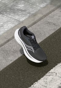 Chaussure de course noire avec une tige texturée, semelle blanche et détails perforés. Présente un logo sur le côté et des lacets pour un maintien sécurisé.