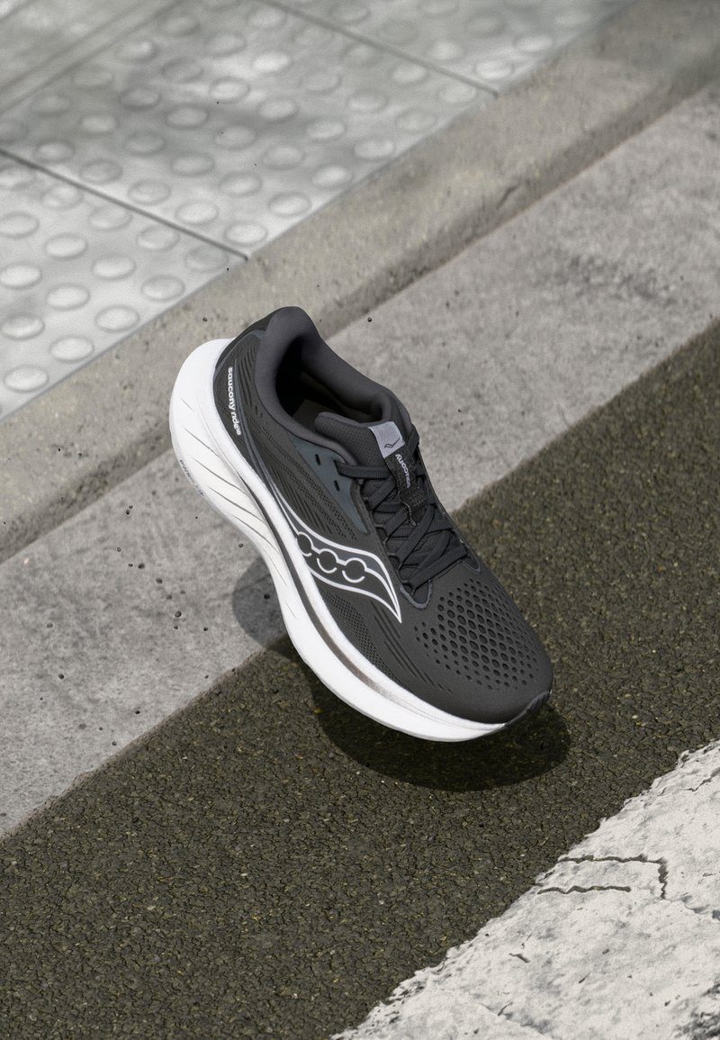 Chaussure de course noire avec une tige texturée, semelle blanche et détails perforés. Présente un logo sur le côté et des lacets pour un maintien sécurisé.