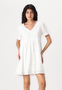 Bílá bavlněná šaty s krátkými rukávy, výstřihem do V a dekorativním vyšívaným vzorem. Vlastnosti zahrnují přední knoflíky a plisovanou sukni.