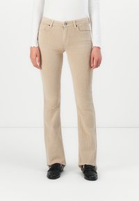 Beige corduroy pants worn with a white long-sleeve top and black lace-up loafers, shown from waist to feet against a plain white background.