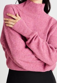 Pull en tricot rose à col roulé avec un col et des poignets côtelés, présentant une finition texturée avec des éclats de couleurs variées. Coupe décontractée.