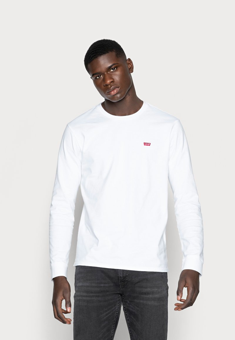 White long-sleeve t-shirt made of cotton with a small red Levi's logo on the chest. Worn with dark gray jeans.