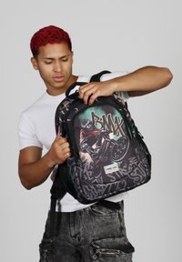 Mochila con un gráfico de BMX que incluye un ciclista, tela negra con patrones de estilo grafiti, correas ajustables y un parche con el logo.